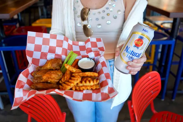 A basket of wings and waffle fries with a cold can