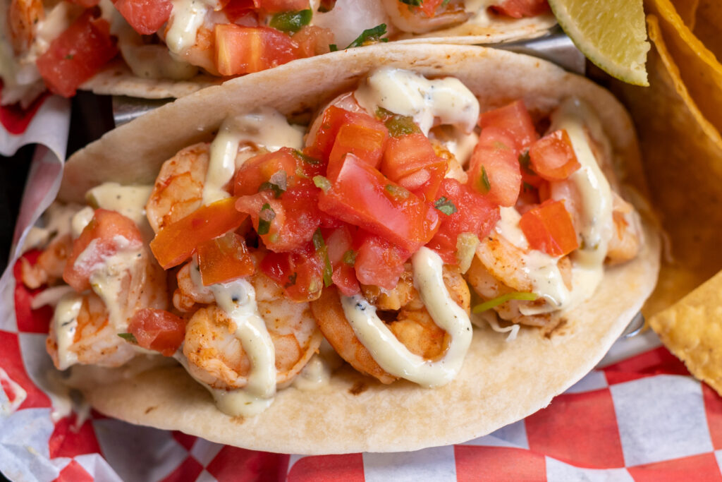 two tacos with shrimp, tomatoes and sauce on them