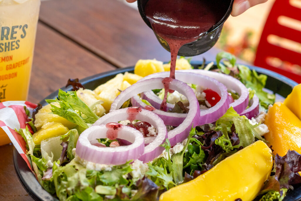 a person pouring dressing on a salad with fruit and vegetables
